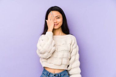 Mor bir arka planda izole edilmiş genç Çinli kadın yüzünün yarısını avuç içiyle kaplayarak eğleniyor..