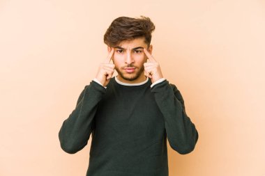 Bej bir arka planda izole edilmiş genç bir Arap adam bir göreve odaklanmış, işaret parmaklarını işaret ediyor..