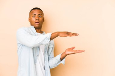 Bej arka planda izole edilmiş genç bir Latin adam elleri arasında bir kopya alanı tutarken şok ve hayrete düştü..