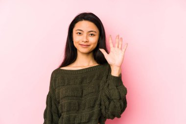 Pembe arka planda izole edilmiş genç Çinli kadın gülümseyerek beş numarayı parmaklarıyla gösteriyor..
