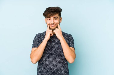 Genç Arap bir adam, iki seçenek arasında şüphe duyan mavi bir arka planda izole edilmiş..