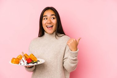 Genç Asyalı kadın bir waffle tutuyor. Parmak kadar uzakta, gülerek ve kaygısızca..