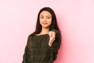 Pembe arka planda izole edilmiş genç Çinli bir kadın selamlaşma jesti olarak kameraya elini uzatıyor..