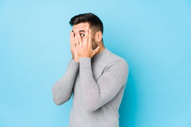 Mavi arka planda genç beyaz bir adam yalnız, korkmuş ve gergin parmaklarıyla göz kırp..