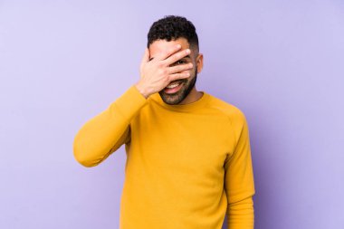 Genç, melez, Arap bir adam kameraya parmaklarıyla göz kırpıyor ve yüzünü kapatmaktan utanıyor..