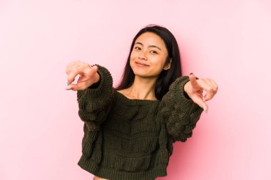 Genç Çinli bir kadın pembe bir arka planda izole edilmiş, mutlu bir şekilde gülümsüyor..