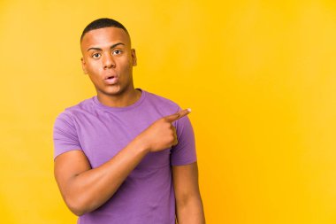 Sarı arka planda izole edilmiş genç latin adam yan tarafı işaret ediyor.