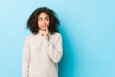 Genç Afro-Amerikan kıvırcık saçlı kadın şüpheli ve şüpheci bir ifadeyle yana bakıyor..