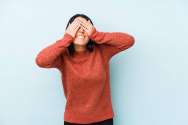 Young caucasian woman isolated on a blue background covers eyes with hands, smiles broadly waiting for a surprise.