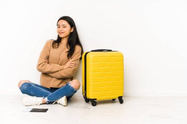 Genç Çinli gezgin kadın, izole edilmiş bir bavulla yerde oturuyor. Kendini güvende hissediyor, kararlılıkla kollarını kavuşturuyor..