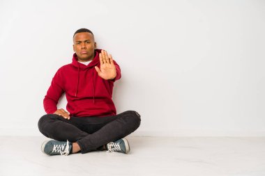 Yerde tek başına oturan genç latin adam elini uzatmış, dur işareti göstererek seni engelliyor..