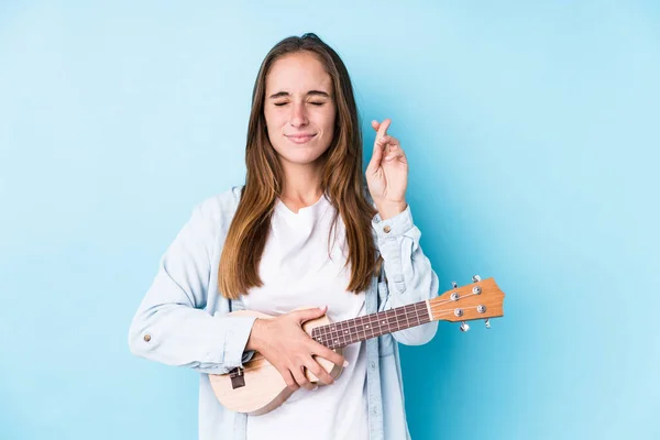 Young Caucasian Woman Holding Ukelele Isolated Crossing Fingers Having Luck — Stock Photo, Image
