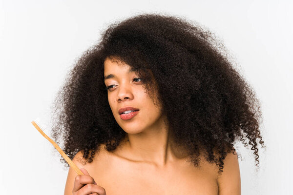 Young afro woman holding a teeth brush isolated looking sideways with doubtful and skeptical expression.