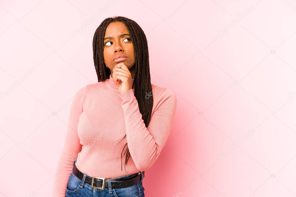 Young african american woman isolated on a pink background looking sideways with doubtful and skeptical expression.