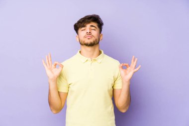 Young arabian man isolated on a purple background relaxes after hard working day, she is performing yoga.