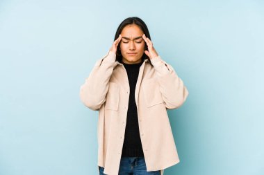 Mavi arka planda izole edilmiş genç bir kadın şakaklara dokunuyor ve baş ağrısı çekiyor..