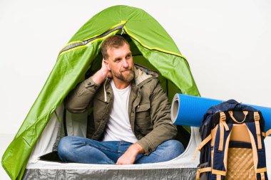 Beyaz arka planda izole edilmiş bir çadırın içinde. Başının arkasına dokunuyor, düşünüyor ve bir seçim yapıyor..