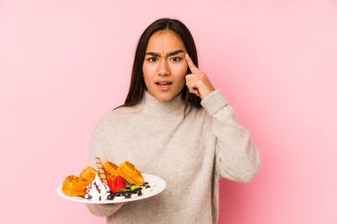 Elinde waffle tutan Asyalı genç bir kadın işaret parmağıyla hayal kırıklığı jesti yapıyor..