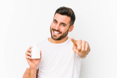 Young caucasian man holding a vitamins bottle isolated cheerful smiles pointing to front.