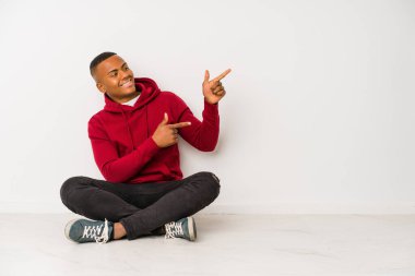 Yerde tek başına oturan genç latin adam işaret parmağıyla işaret ederek heyecanlanıyor..