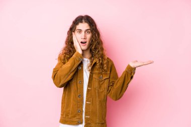 Uzun saçlı, yalnız poz veren genç bir adam avucunun içinde fotokopi alanı tutuyor, el üstünde tutuyor. Şaşırmış ve mutlu..