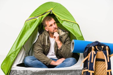 Beyaz arka planda izole edilmiş bir çadırın içinde şüpheli ve şüpheci bir ifadeyle yan tarafa bakıyor..