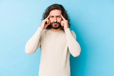 Uzun saçlı genç adam mavi bir arka planda izole edilmiş bir vazifeye odaklanmış, işaret parmaklarını işaret ediyor..