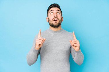 Mavi arka planı olan beyaz bir genç, ağzı açık, üst tarafı göstererek izole edilmiş..