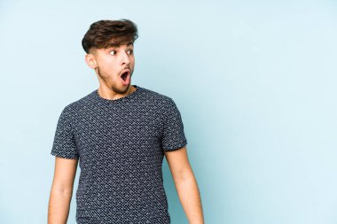 Genç Arap bir adam mavi bir arka planda izole edilmiş. Gördüğü bir şey yüzünden şok oluyor..