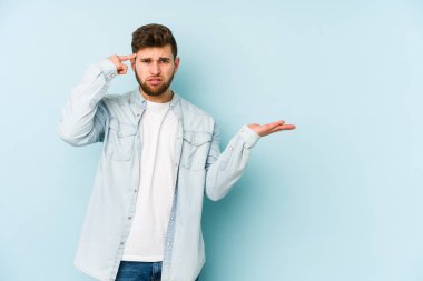 Kafkasyalı genç adam mavi arka planda izole edilmiş ve elinde bir ürün tutuyor..