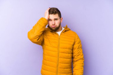 Mor arka planda soyutlanmış genç bir adam yorgun ve uykulu. Elini başının üstünde tutuyor..