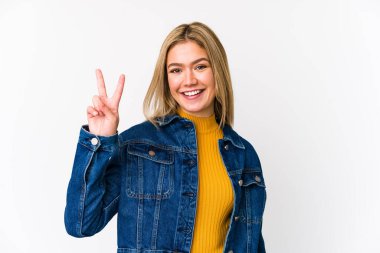 Sarışın, beyaz tenli, izole bir kadın zafer işareti gösteriyor ve gülümsüyor..