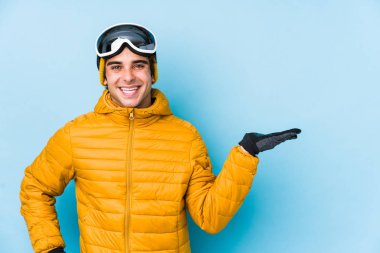 Snowboard gözlüğü takan genç kayakçı avucunun içinde bir fotokopi alanı gösteriyor ve belinde başka bir el tutuyor..