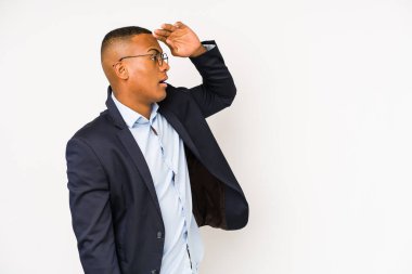 Genç iş adamı beyaz arka planda soyutlanmış, uzaklara bakıyor ve elini alnına koyuyor..