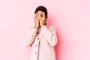 Pembe arka planda poz veren beyaz bir genç parmaklarıyla korkmuş ve gergin bir şekilde göz kırpıyor..