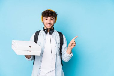 Elinde pizza tutan genç Arap öğrenci gülümseyip işaret ediyor, boş alanda bir şey gösteriyor..