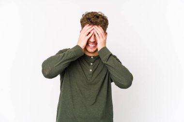 Sarışın, kıvırcık saçlı, beyaz tenli bir adam izole edilmiş, gözleri ellerle kaplanmış, gülümseyerek bir sürpriz bekliyor..