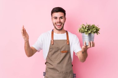 Kafkasyalı genç bahçıvan elinde bir bitki tutuyor. Hoş bir sürpriz bekliyor. Heyecanlı ve el kaldırıyor..