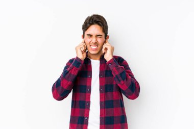 Pembe arka planda poz veren genç beyaz bir adam kulaklarını elleriyle kapatıyor..