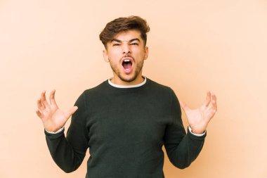 Genç Arap adam bej bir arka planda izole edilmiş öfkeyle bağırıyor..