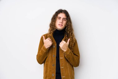 Uzun saçlı adam yalnız poz veriyor. Baş parmağını kaldırıyor, gülümsüyor ve kendinden emin..