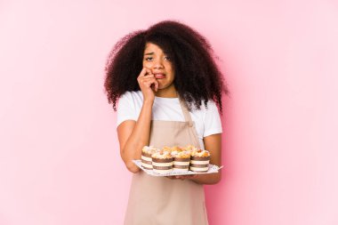 Elinde kek tutan genç afro pastacı kadın tırnak yiyen genç afro fırıncı kadın gergin ve çok endişeli..