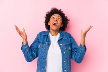 Genç Afrikalı Amerikalı bir kadın pembe bir arka plana karşı gökyüzüne doğru çığlıklar atıyor, bakıyor, hayal kırıklığına uğruyor..