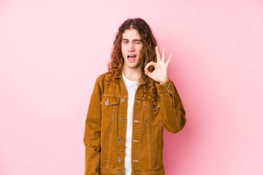 Genç, uzun saçlı, yalnız poz veren bir adam bir göz kırptı ve elleriyle iyi bir jest yaptı..