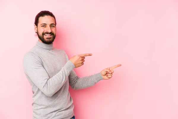 Giovane Uomo Capelli Lunghi Isolato Uno Sfondo Rosa Eccitato Indicando — Foto Stock