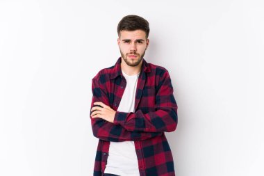 Beyaz arka planda poz veren beyaz tenli, hoşnutsuzca somurtan, kollarını kavuşturan genç bir adam..