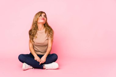 Genç sarışın beyaz kadın pembe bir stüdyoda oturmuş amaçlarına ve amaçlarına ulaşmanın hayalini kuruyor.