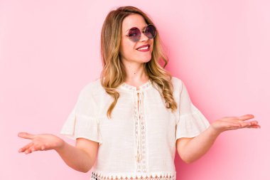 Pembe arka planda gözlüklü genç beyaz kadın kollarıyla ölçeği yapıyor, mutlu ve kendinden emin hissediyor..