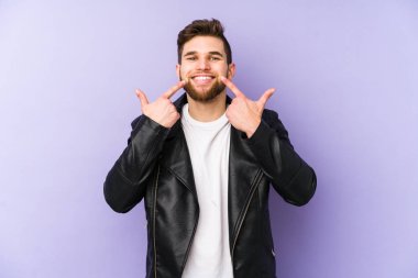 Mor arka planda izole olmuş genç adam gülümsüyor, parmaklarını ağıza doğrultuyor..