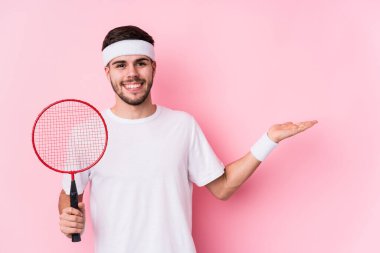 Badminton oynayan beyaz bir adam avuçta fotokopi alanı gösterip belinde bir el daha tutuyor..